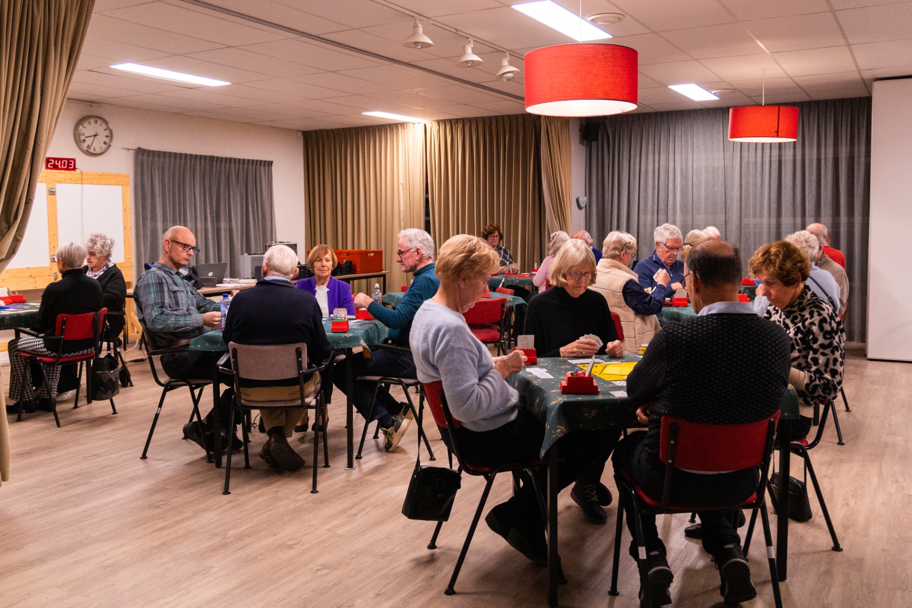 Overzicht van de speelzaal in Het Trefpunt met bridgende leden aan meerdere tafels